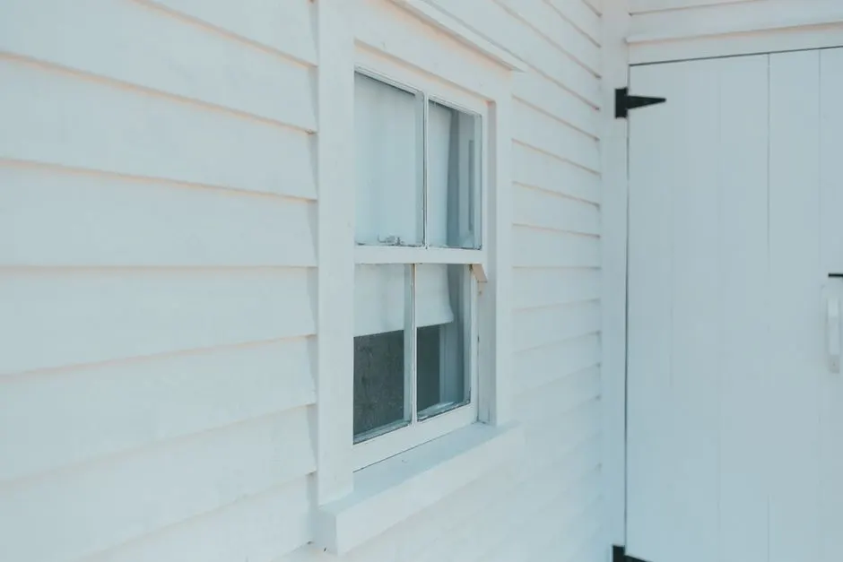 Close-up of a white wooden facade showcasing a window and door, highlighting minimalist architecture.